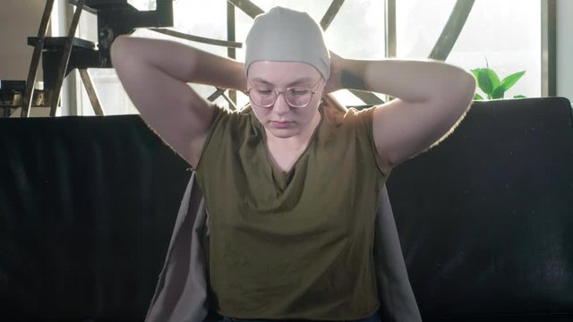 Portrait of pale woman sick with cancer, request for help, social protection. A bald girl with cancer or leukemia puts a scarf on her head. Tie fabric on head. She completed a course of chemotherapy.