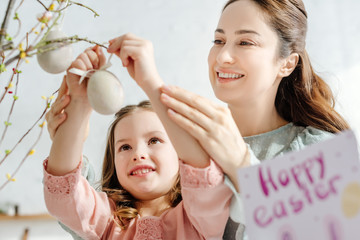 selective focus of smiling mother and daughter looking at decorative easter eggs