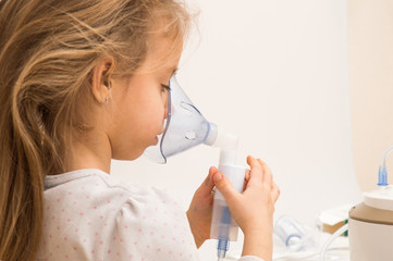 Close up. Respiratory diseases. A little girl holds a nebulizer nozzle and inhales the medicine....