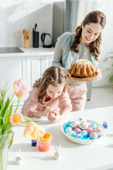 selective focus of kid painting chicken egg and mother with easter cake
