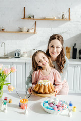 Fototapeta na wymiar Happy child and mother near easter eggs, decorative rabbits, easter bread and tulips