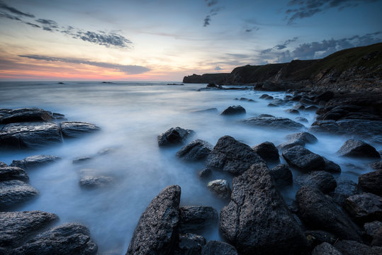 Amazing long exposure seascape with rocky beach at sunrise in the blue hour