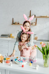 Happy mother hugging daughter in bunny ears near easter eggs
