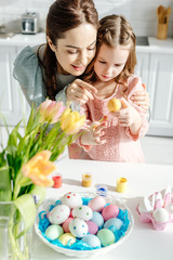 Obraz na płótnie Canvas selective focus of happy mother and cute daughter looking at easter egg near tulips