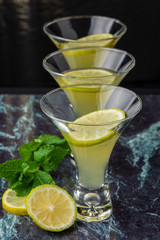 Top view of three glasses of mojito with lime and mint slices on blue marble and dark vertical background
