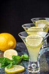Close-up of three glasses of mojito, with selective focus, with lemon, lime wedges and mint on blue marble and vertical black background
