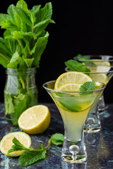 Top view of three glasses of mojito, with selective focus, with lime wedges and sprig of mint on blue marble and black background in vertical