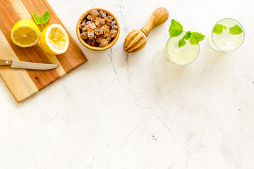 Homemade lemonade in glasses near juicer and cut lemons on white background top-down copy space