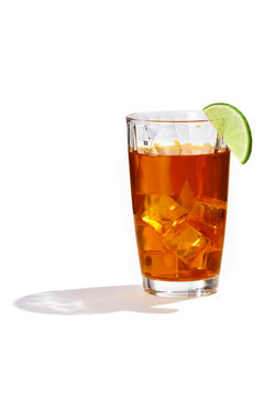 Long Island cocktail with ice cubes is contained in a highball glass with a lime slice on the rim and a straw. The showy illustrative picture is made on the white backdrop.