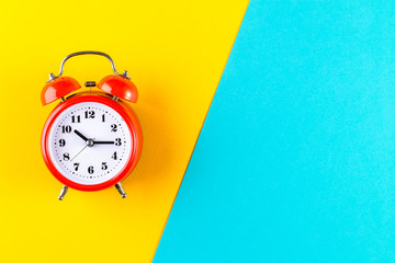 Red vintage alarm clock on a blue and yellow background. Alarm clock with place for text. Time...