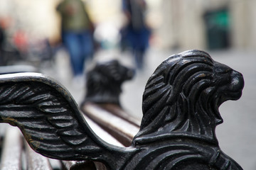 Lion's head sculpture on bench handrail. Lion with wings. - 331209756
