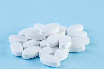 Heap of white medical pills on a light blue background. Pharmaceutical medicament, cure for health....