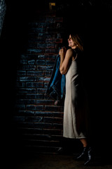 brunette girl in a green jacket and bra stands near the white brick wall.