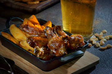 chicken wings in teriyaki sauce with potato slices and a glass of beer