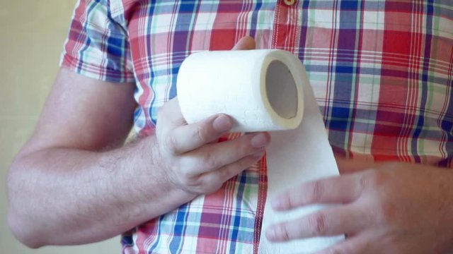 Men's hands unwind a roll of white toilet paper.