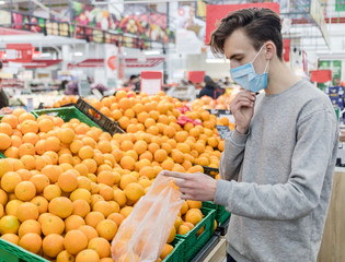 Young man wearing disposable medical mask shopping in supermarket during coronavirus