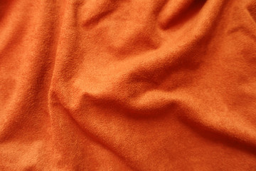 Surface of bright reddish orange artificial suede fabric in soft folds
