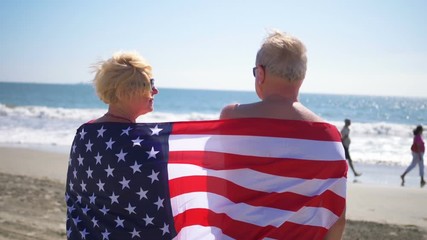 Seniors couple hugging on the beach wrapped up with American flag in slow motion 180fps - Powered by Adobe