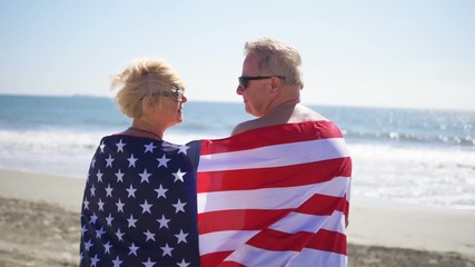 Seniors couple hugging on the beach wrapped up with USA flag in slow motion 180fps - Powered by Adobe