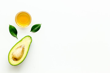 Avocado oil - for cooking - in glass bowl near halfs of vegetable on white background top-down frame copy space