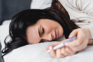 selective focus of woman lying on bed and holding pregnancy test with negative result