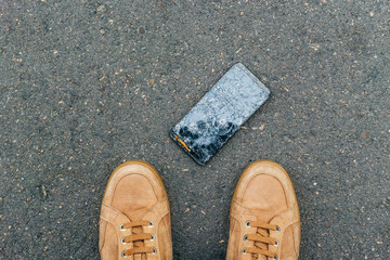 Cell phone dropped on the floor with its owner staring at the phone with its screen broken.