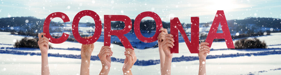 People Hands Holding Red English Word Corona. Snowy Winter Background With Snowflakes