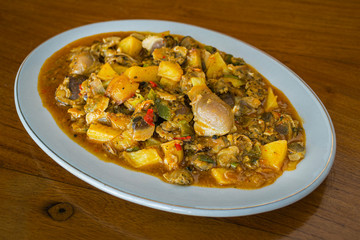 Kerang saus padang is Indonesia food made from mussels, potato,  chili sauce, tomato sauce, garlic and other ingredients. has a savory and spicy taste. in white plate on wooden background