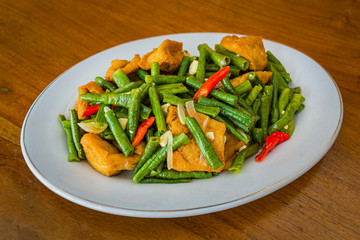 Tumis tahu kacang panjang is Indonesia food made from fresh long beans, tofu, cayenne pepper and other ingredients which is cooked by stir-frying. in white plate on wooden background