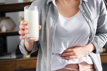 cropped view of woman with lactose intolerance holding glass of milk while touching stomach