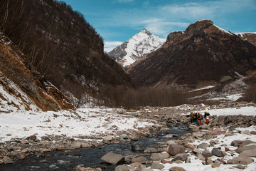group of traveling people with ski equipment walks along mountain river.