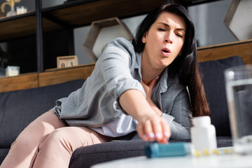 selective focus of woman with asthma coughing while reaching for inhaler