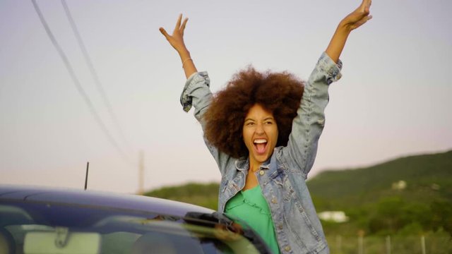 Slow motion shot of young woman during road trip with raised arms