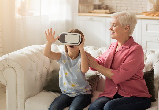 Smiling mature lady and her granddaughter in virtual reality headset at home