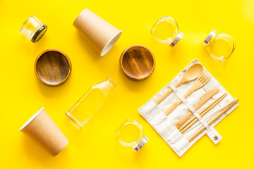 Set of eco friendly bamboo tableware, cotton bag, paper mug and glass jars. Sustainable lifestyle, plastic free concept on yellow table - top view