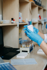 Blood test process in laboratory. Doctor hands making blood test. Many blood test-tubes with blood on the table. Covid-19 testing.