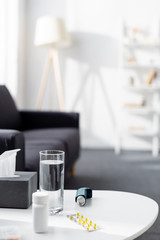 glass of water near tissue box, inhaler and blister pack with pills