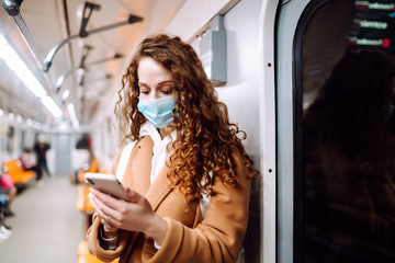 Girl in protective sterile medical mask on her face with a phone in a subway car. Woman using the phone to search for news about coronavirus. The concept of preventing the spread of the epidemic.