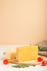 Various types of cheese with rosemary and tomatoes on wooden board on a white and orange background. Side view, copy space.