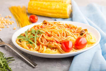 Corn noodles with tomato sauce and arugula on a gray concrete background. Side view, selective focus.