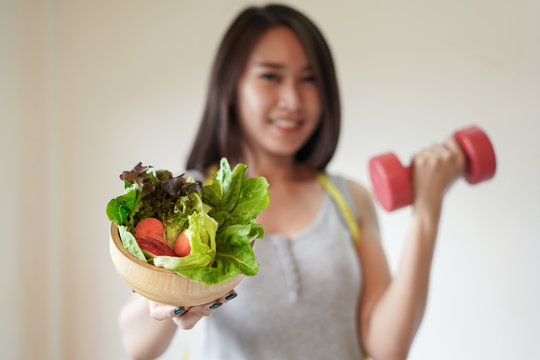 Healthy slim woman holding salad bowl and dumbbell with happy face and lifestyle diet, fitness and healthy concept.