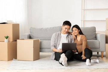 Young asian couple using laptop sitting on floor