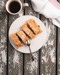 Strudel on a white plate on a wooden backdrop, a dessert, coffee in a cup, vintage spoon
