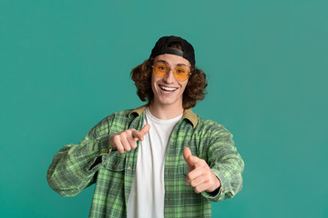 Portrait of cool young guy in sunglasses pointing at you on color background
