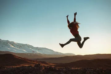Fotobehang Gelukkig meisje springt tegen bergen bij zonsondergang © cppzone
