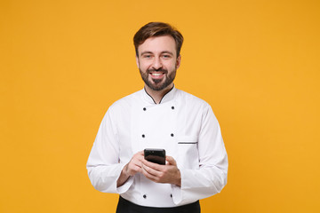 Smiling young bearded male chef cook or baker man in white uniform shirt posing isolated on yellow...