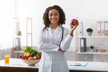 Pretty black lady dietologist holding apple in her hand - obrazy, fototapety, plakaty