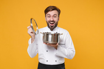 Excited young bearded male chef cook or baker man in white uniform shirt posing isolated on yellow...