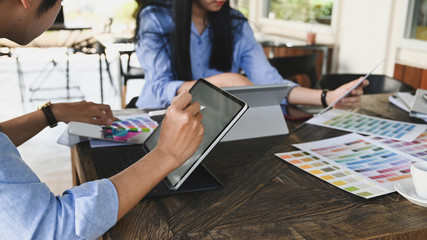 Cropped image of graphic designer team working together with computer tablet and color guide/information at the wooden meeting table over vintage office as background.