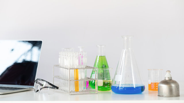 Photo of Scientific equipment, chemistry glassware and computer laptop putting together on white working desk over laboratory white wall as background.